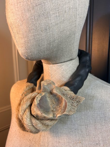 A textured necklace featuring a large fabric flower and a dark leather strap.