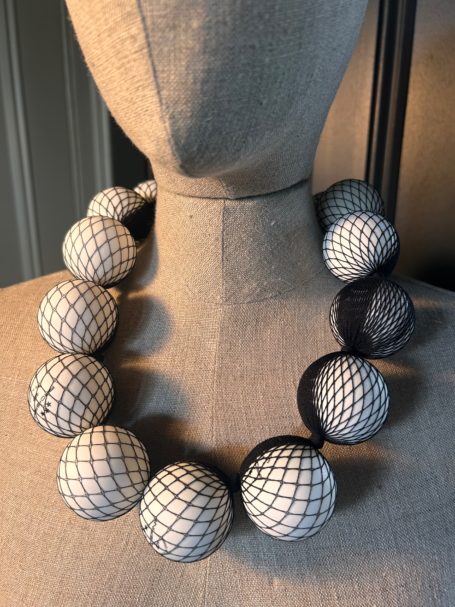 Large decorative necklace featuring spherical beads in a netted design, displayed on a mannequin.